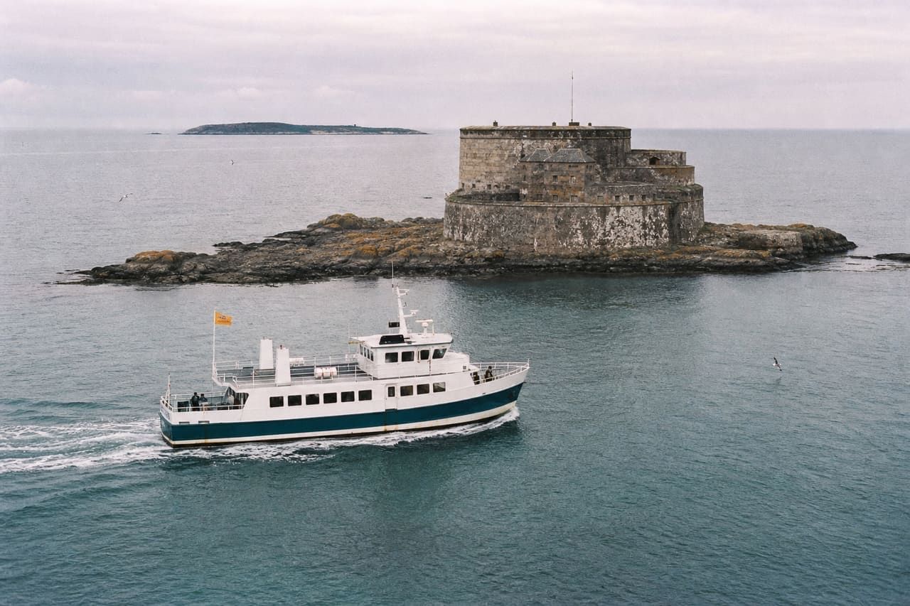 A white and teal Lietvirk ferry passing the stone walls of the Miren fortress at sea