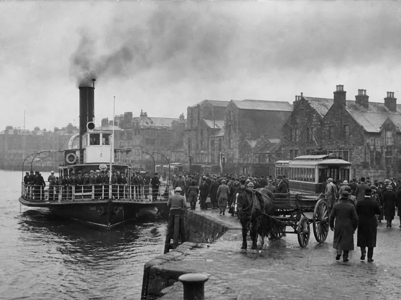 A sepia photograph from 1931 of a crowded steam ferry leaving a stone pier, passengers in hats at the rail and the Old Town cathedral spire behind