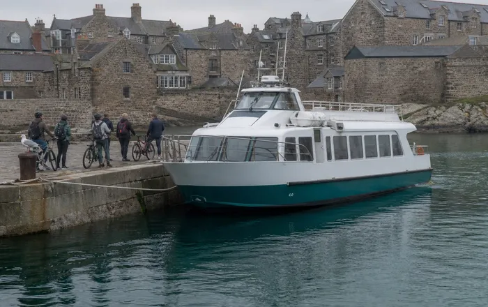 A white and teal Harbour Ferry moored at the granite quay at Selsta Ost with commuters and bicycles waiting