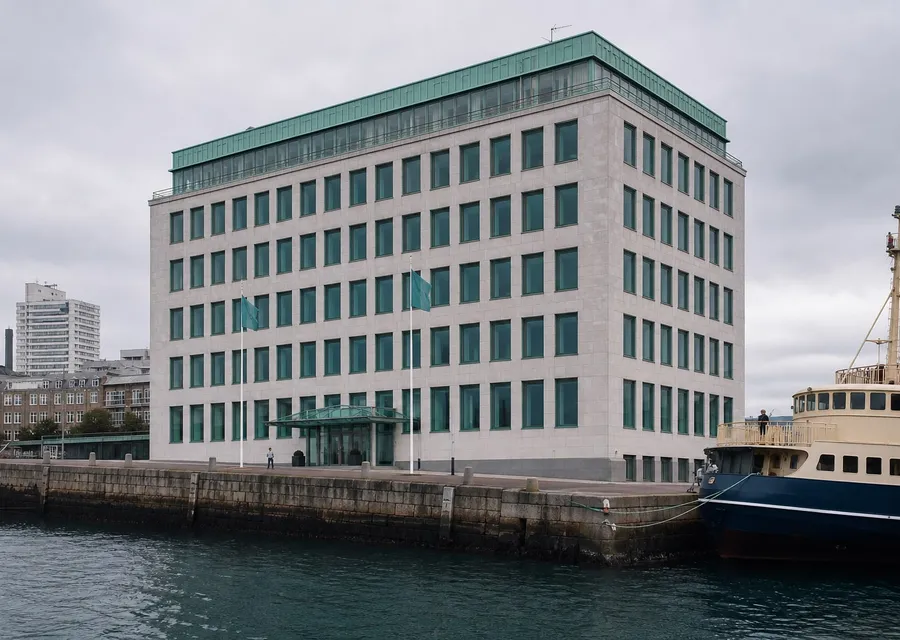Veikavan House, a five-storey harbour-front building of pale stone on Nevost Quay, with the ring-and-wave mark above the entrance and a ferry moored alongside