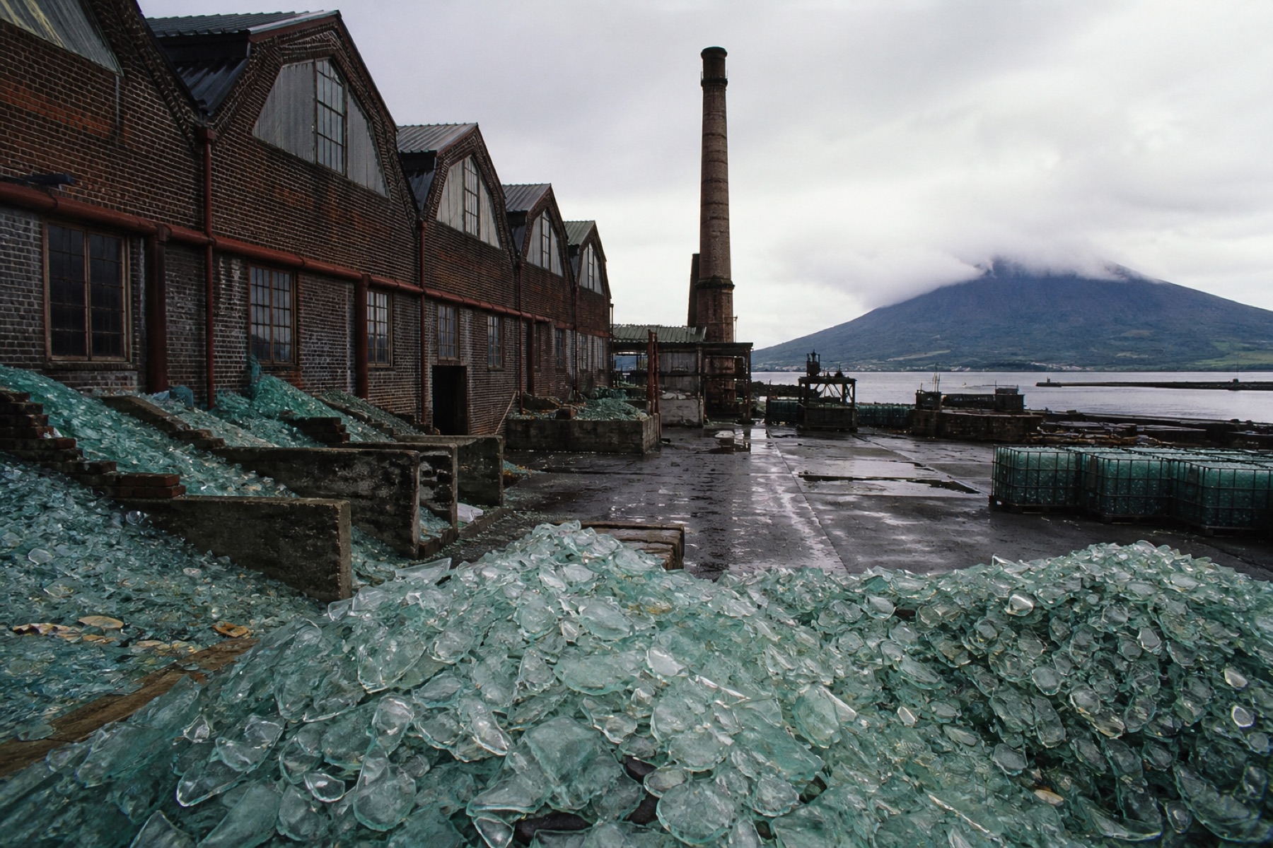 Historic glassworks sheds and a yard of pale green cullet opening toward the harbour.